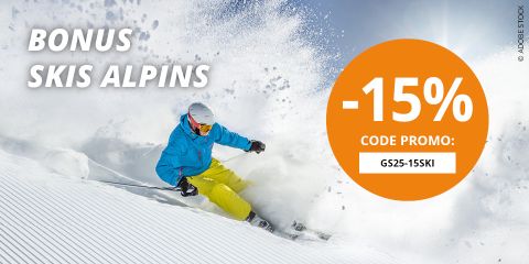 Un skieur en veste bleue et pantalon jaune dévale une piste enneigée. Le texte indique : « BONUS SKIS ALPINS » et un grand cercle orange offre « -15% CODE PROMO : GS25-15SKI ». La neige gicle de façon spectaculaire en arrière-plan.