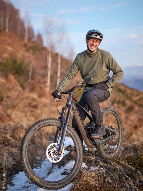 Une personne avec un casque et une veste verte sourit en posant avec un VTT sur 